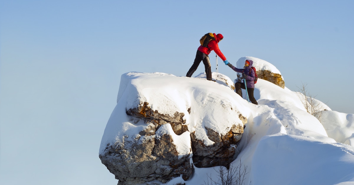 two-hikers-top-mountain-winter-man-helps-woman-climb-sheer-stone