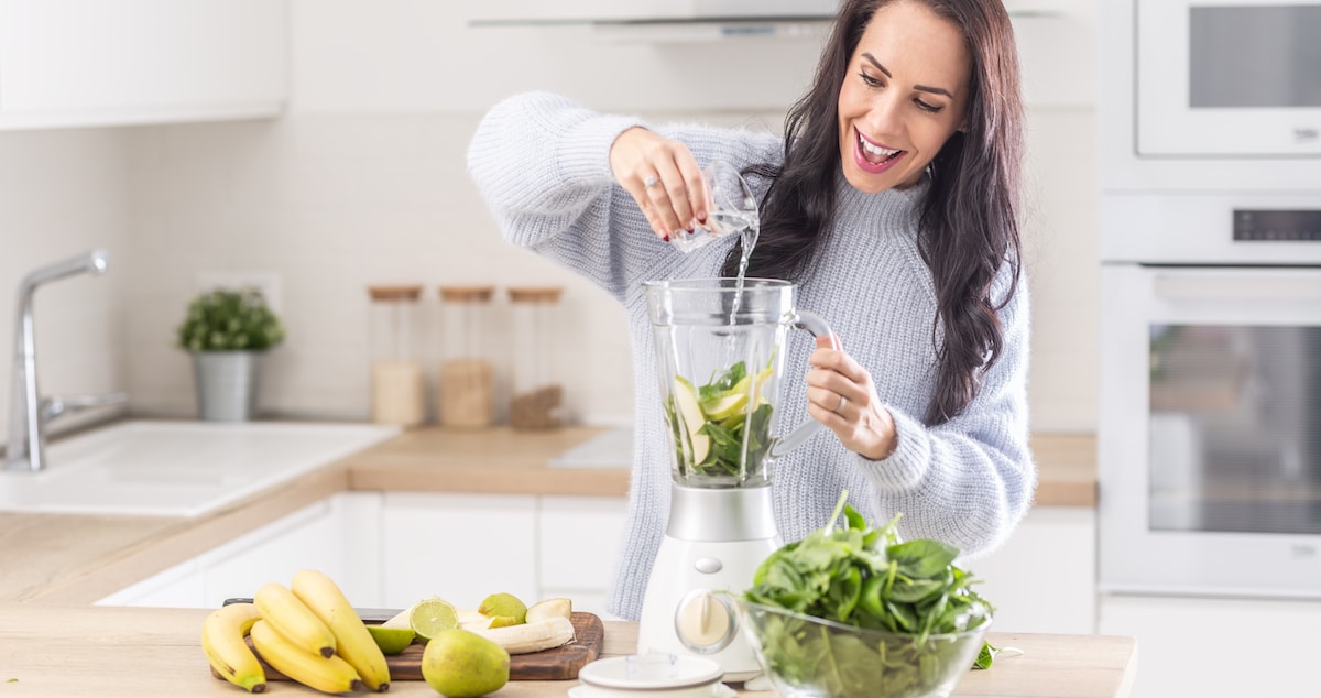 woman-adds-water-into-mixer-spinach-banana-apple-smoothie
