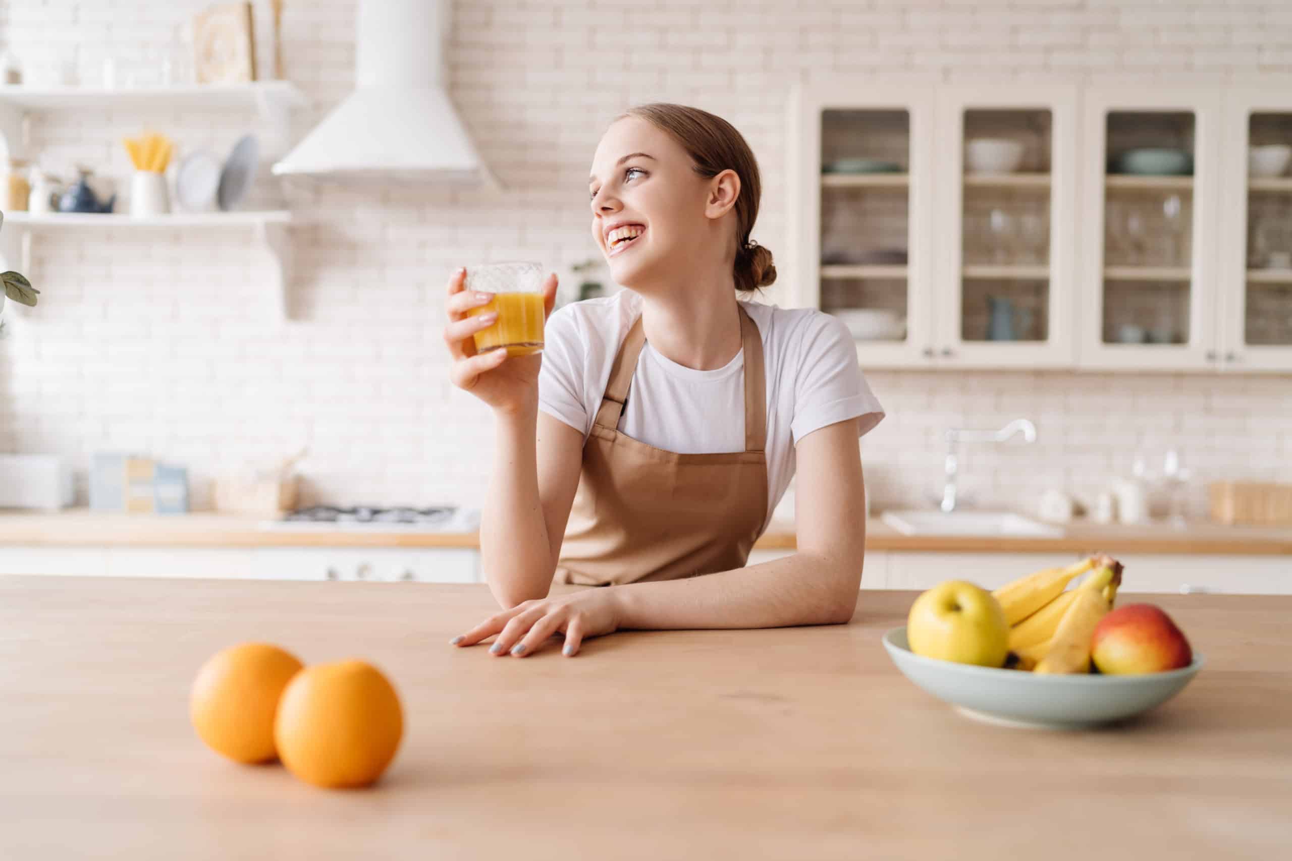 young-beautiful-woman-kitchen-apron-fruits-orange-juice-scaled