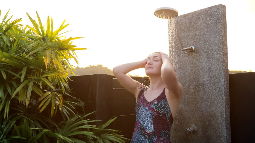 brunette-washes-long-loose-hair-pool-outdoor-shower-concrete-support-near-tropical-tree-back-bright-summer-sunlight-1024x576