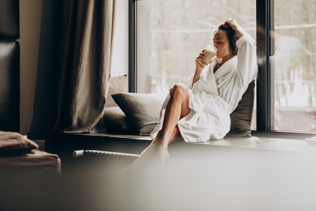 woman-drinking-coffee-bathrobe-by-window-home-1024x683